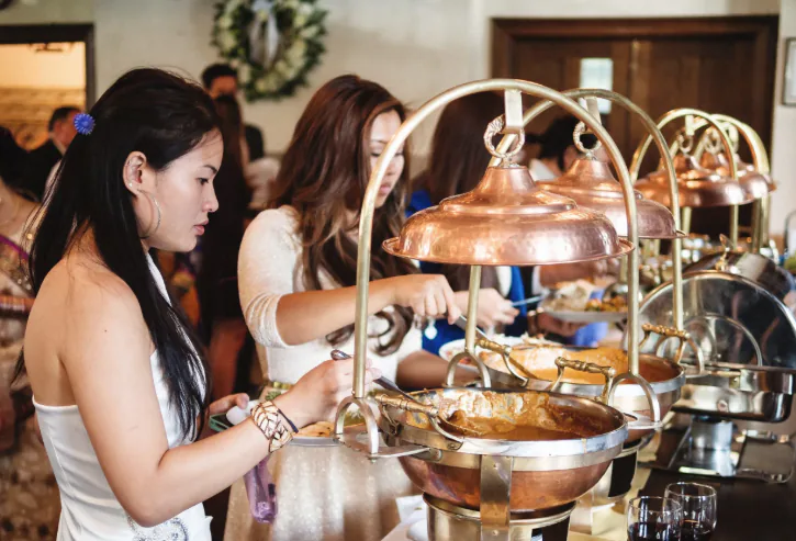Guests serving themselves from copper buffet warmers at an indoor catered event
