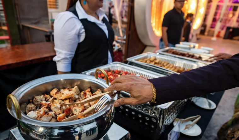 Outdoor catered buffet trays with guests and service staff nearby
